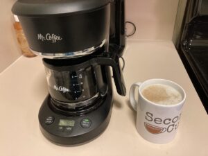 A Mr. Coffee 5-cup coffee maker and a mug full of coffee.